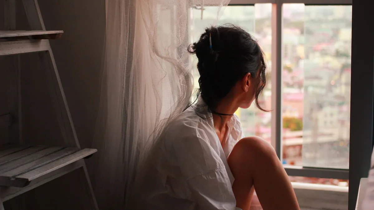 A woman sitting in soft daylight looking out of a window