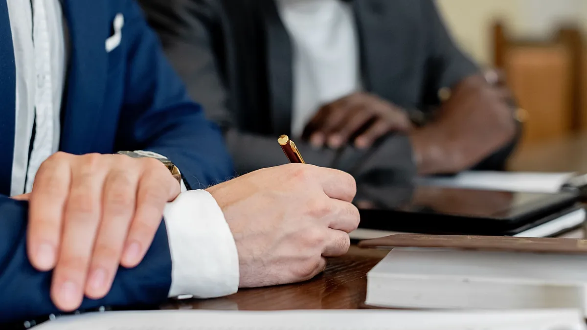 Hands folded on a meeting table while someone takes notes