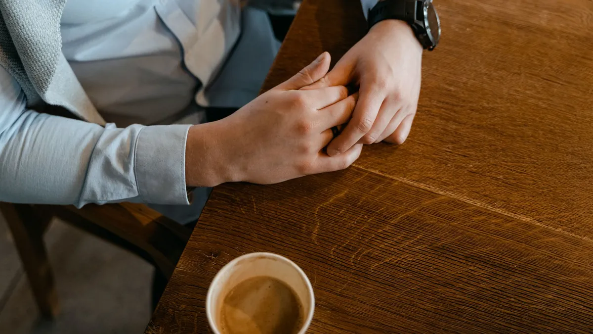 Hands resting quietly on a desk next to a cup of coffee, seen from above
