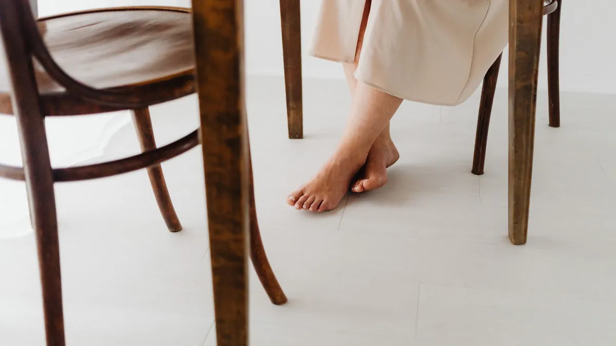 Bare feet resting flat on the floor beside a wooden chair