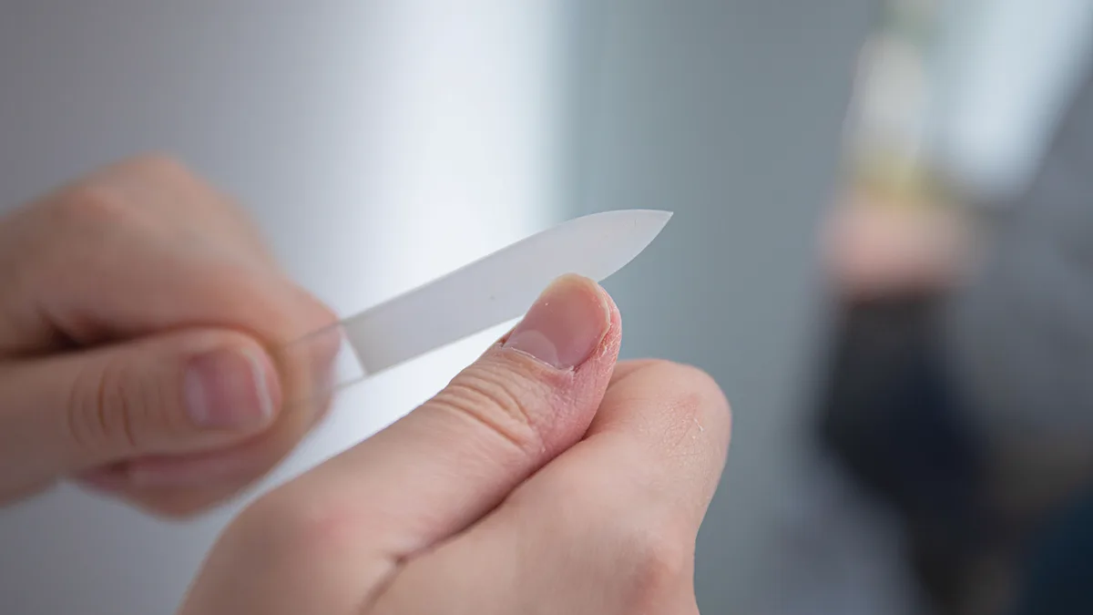 A glass nail file smoothing the edge of a thumbnail