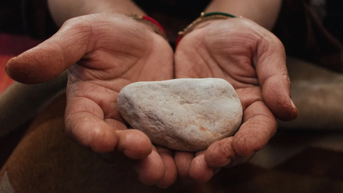 Two cupped hands gently holding a single smooth pale stone